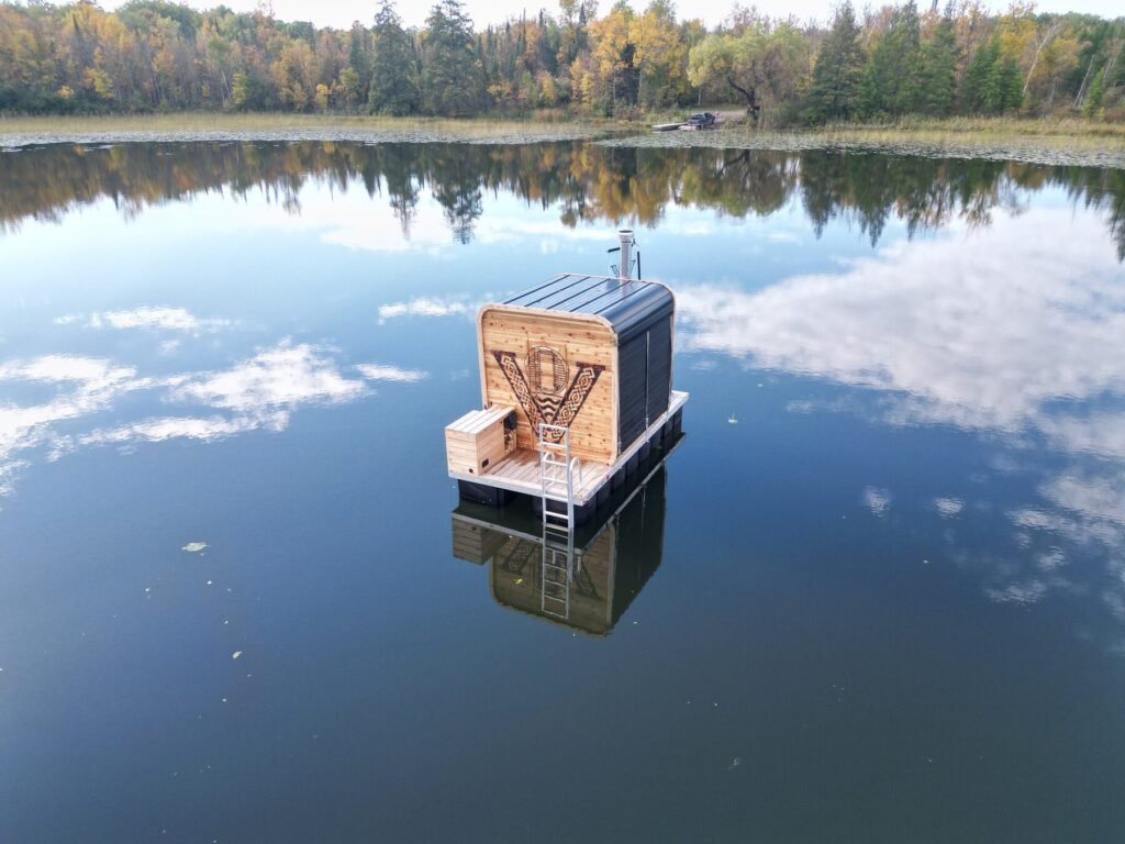 Valhallan floating sauna on a still lake reflecting clouds and fall trees