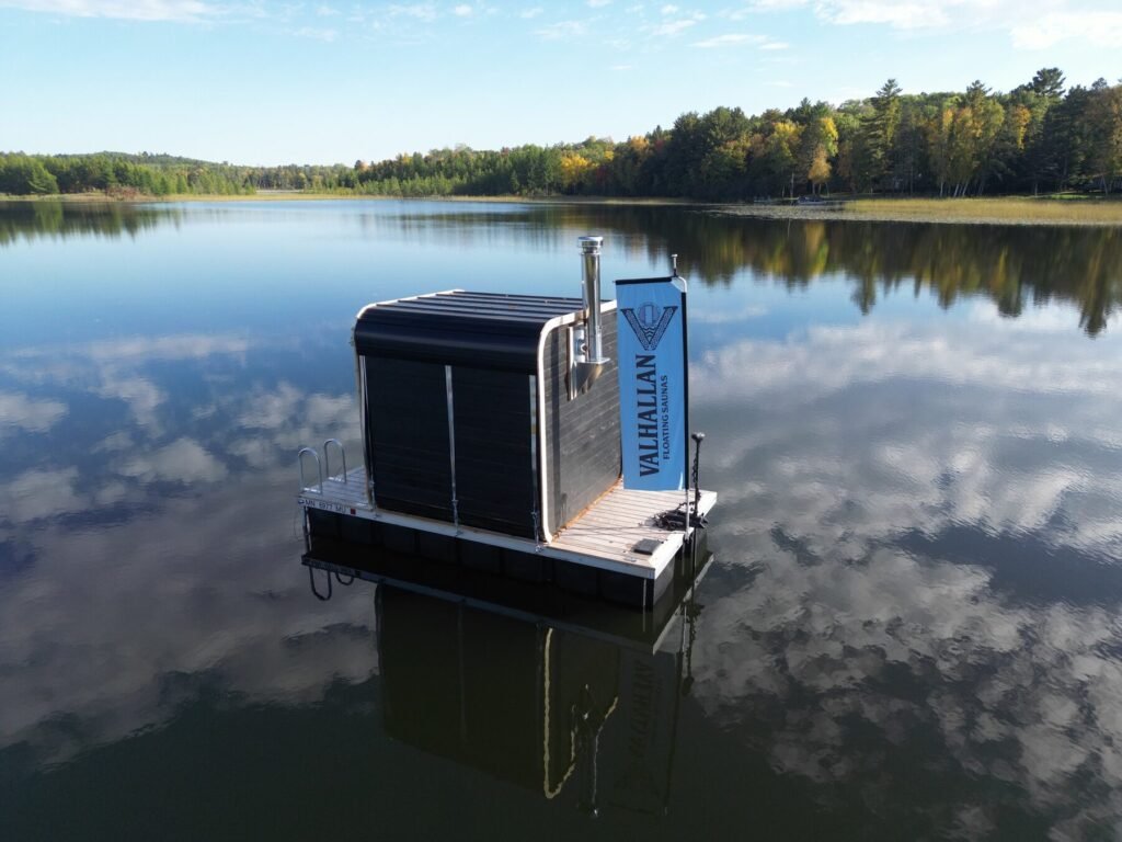 Back of the Valhallan floating sauna with the Valhallan banner on a calm lake